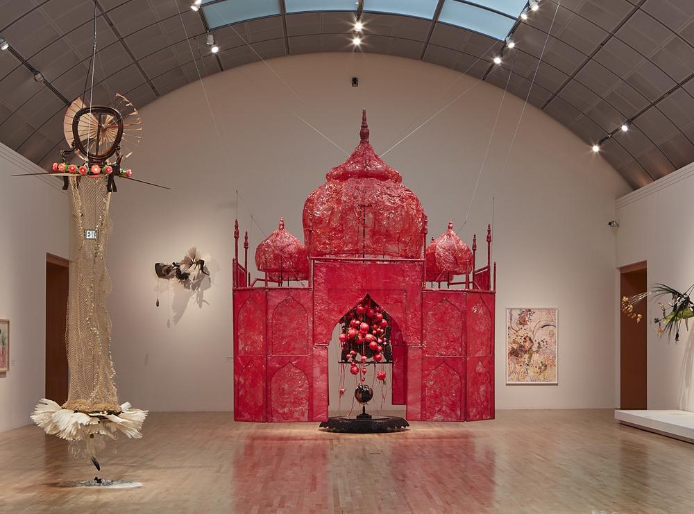 Mixed media sculpture in bright pink plastic wrap resembling the Taj Mahal. It is suspended from a vaulted ceiling.