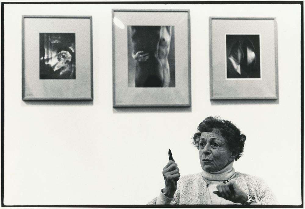 artist talking in front of three photographs hung on a gallery wall over her head