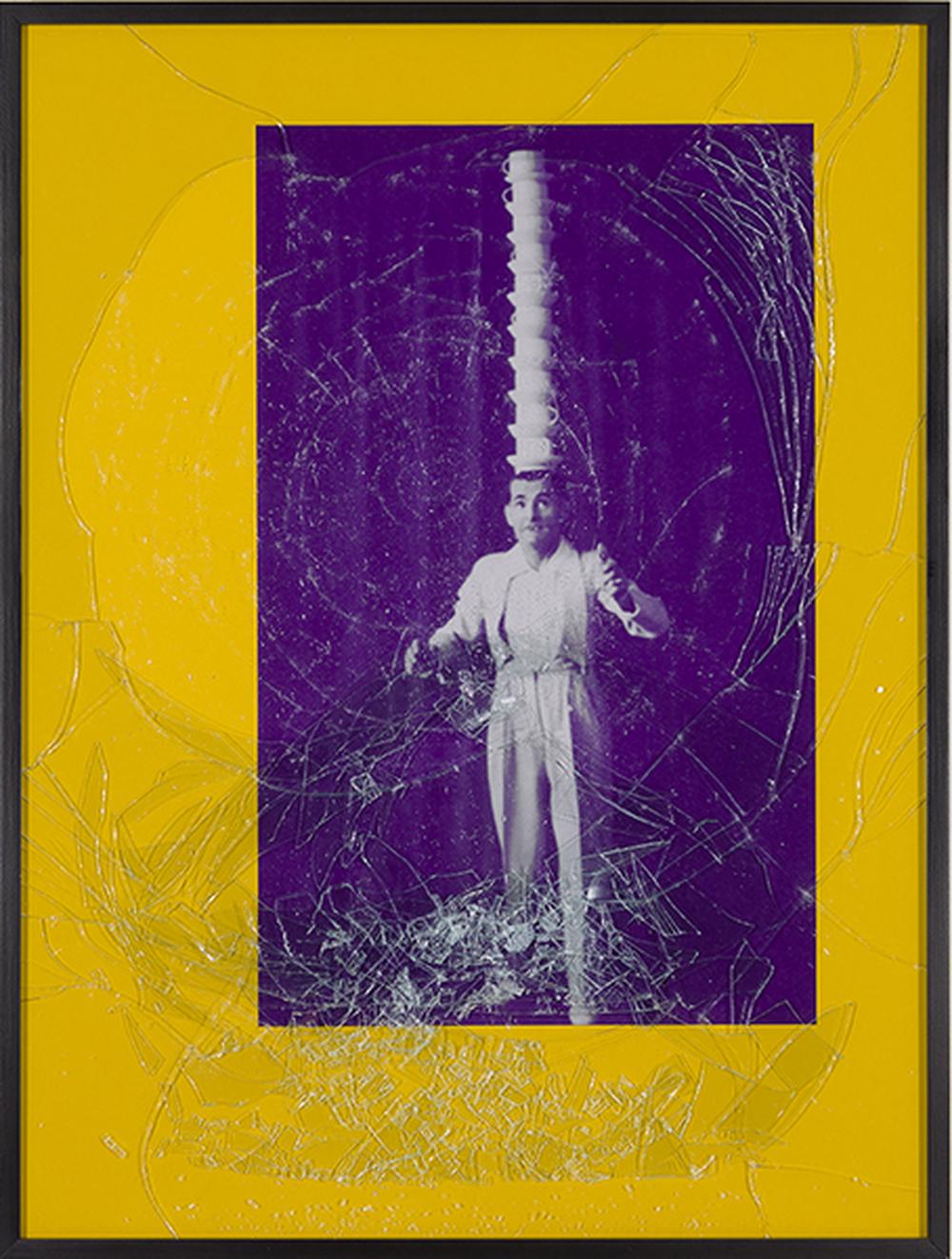 a man in a suit balancing a tower of 10 teacups and saucers on his head in a frame with cracked glass