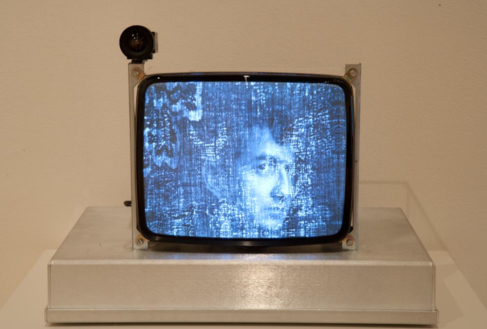 video monitor with grainy blue and white image of a white male face