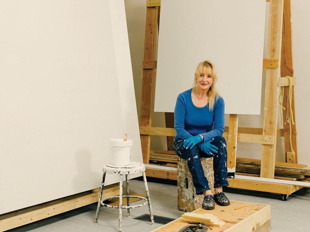 Woman sitting on stool in a painting studio in front of large blank canvases