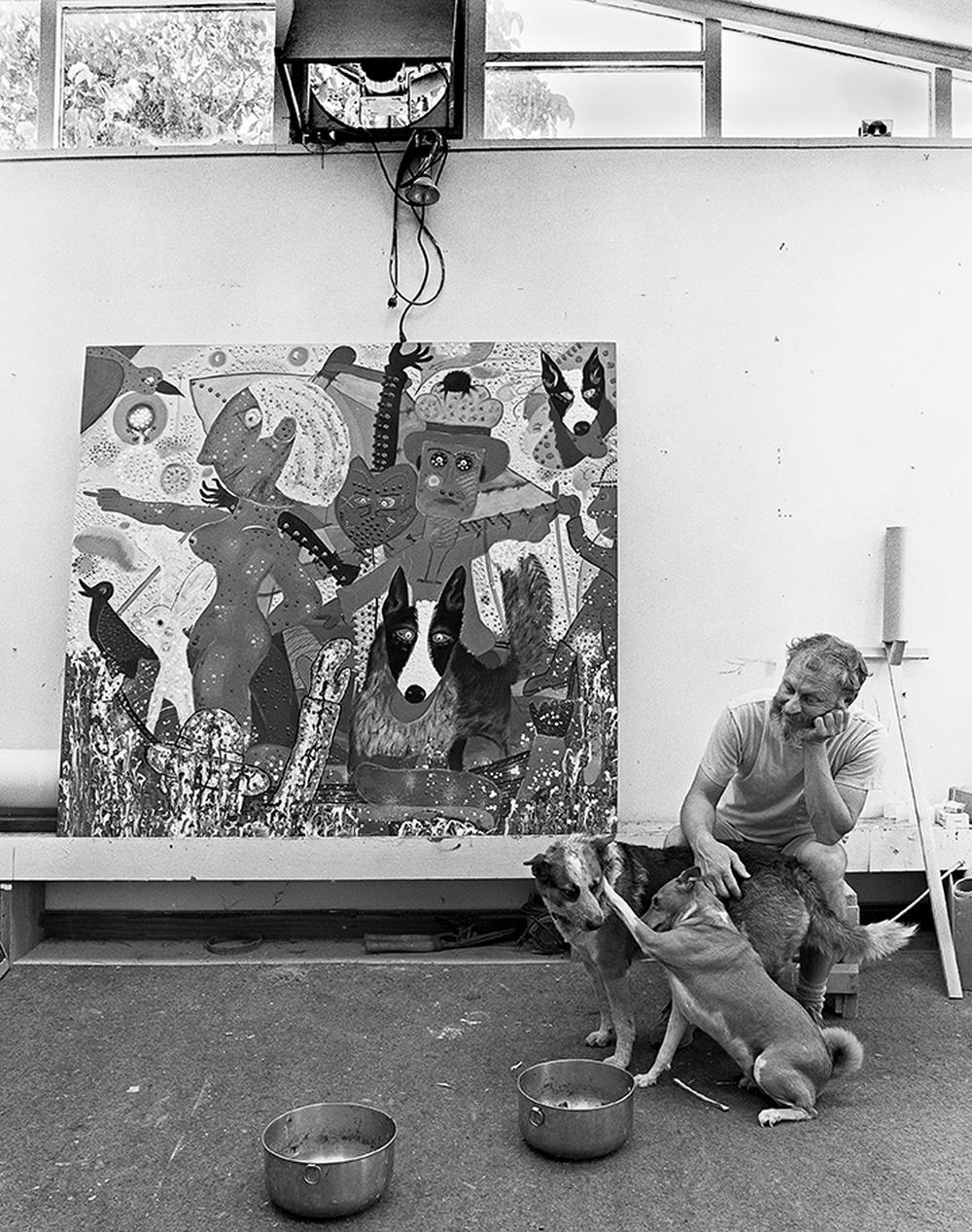 artist in his studio with large painting in the background and his two dogs in the foreground