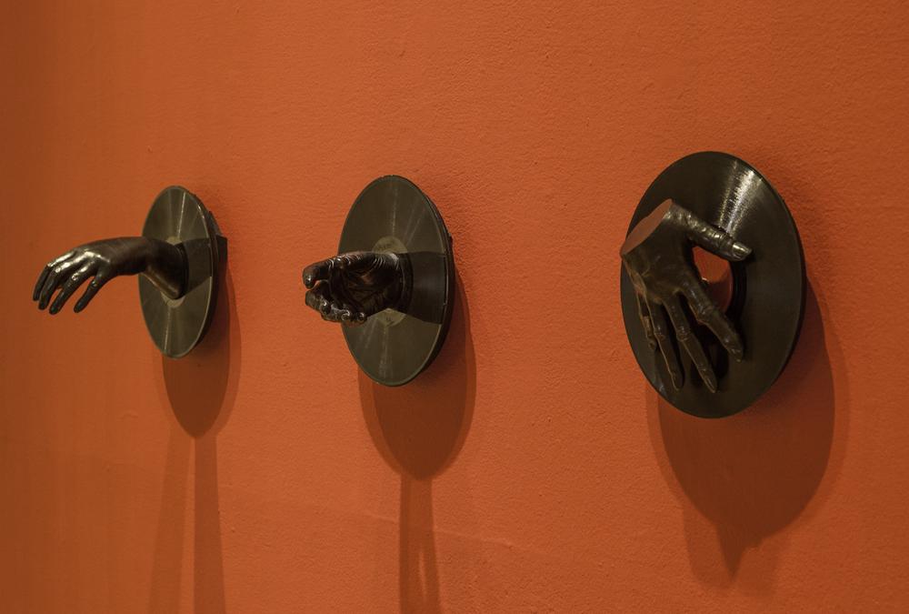 three pieced sculpture of a a right hand interacting with three different records in different ways