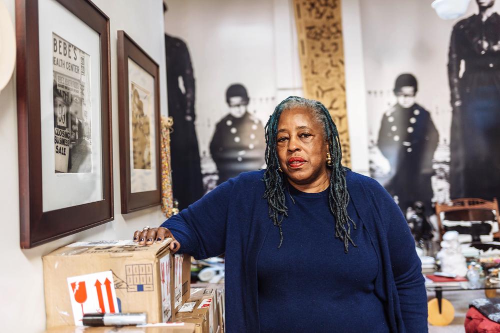 black woman sitting in room surrounded by books, artwork, and art supplies