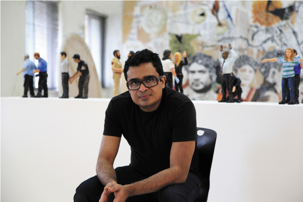 Artist sitting in studio with sculptures and paintings in the background