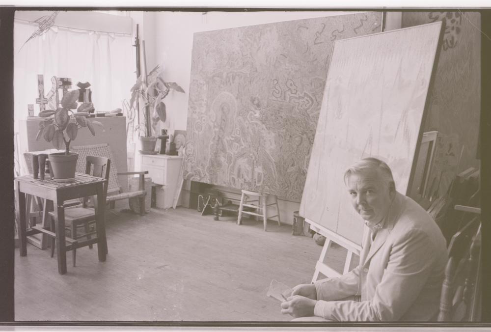 man sitting in the bottom right of a view into his studio of large canvases