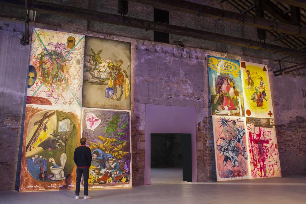 person standing in front of artworks on a large wall that cover it from ceiling to floor