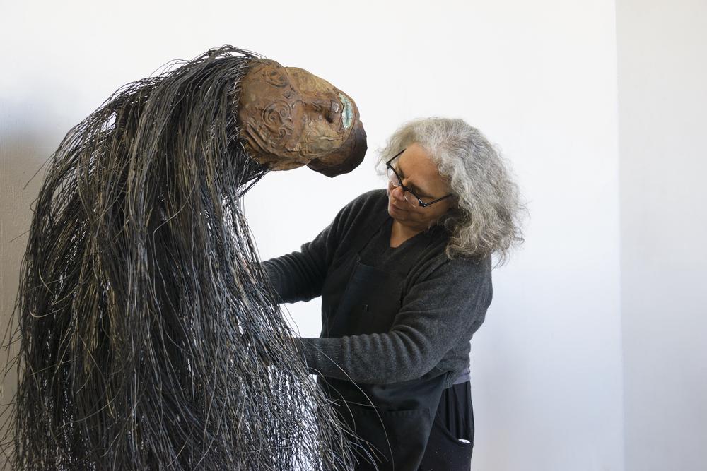 artist working on sculpture of large head balancing on a large mass of hair coming out of the head