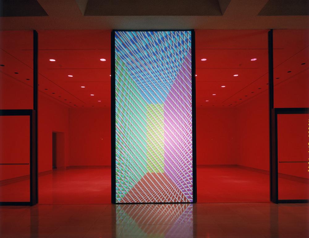 a red lit empty gallery behind a projected display of blue green red yellow and pink blocks of color