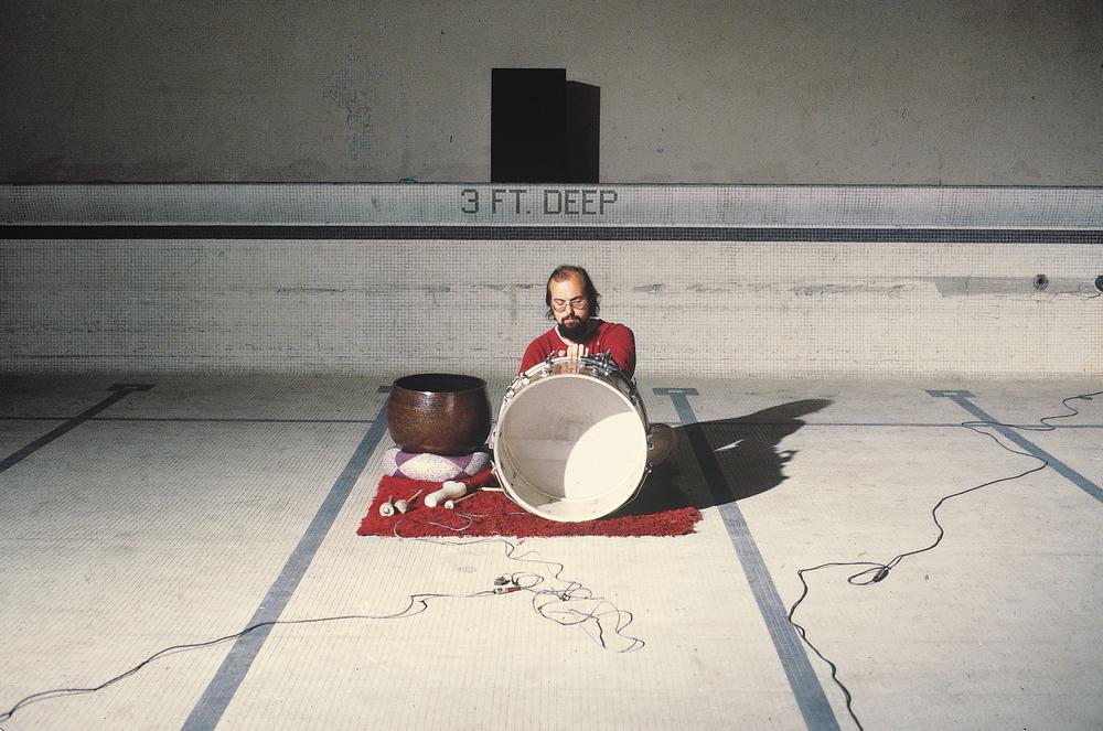 white man sitting at the bottom of an empty pool playing the drums